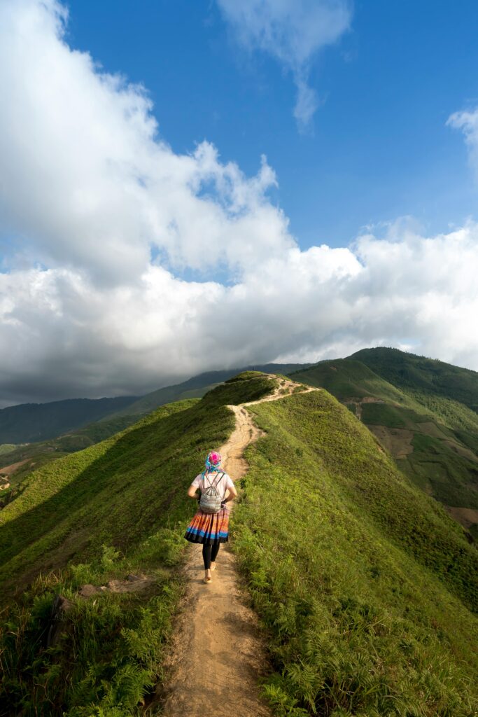 pexels-photo-2132126-2132126 A lone hiker walking on a scenic mountain trail surrounded by lush greenery and clear blue skies.